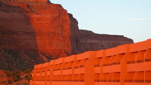 A large, orange building with a unique architectural design, situated in a desert landscape with red rock formations in the background. - The View Hotel (Oljato-Monument Valley)