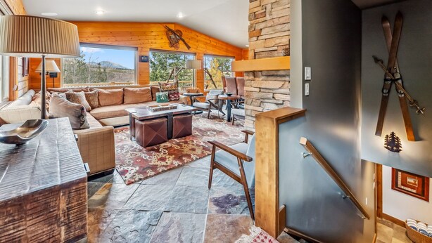 Amplio salón con chimenea de piedra, paredes de madera y un ventanal con vistas a un paisaje montañoso.