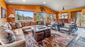 Interior acogedor de una cabaña de madera con un sofá grande, una mesa de centro y una zona de comedor con sillas.
