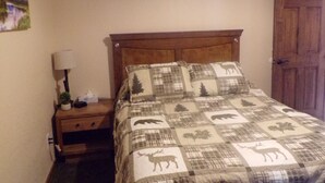 A bedroom with a bed, a nightstand, a lamp, a painting of a mountain landscape, and a wooden door. - 30 miles from Breck!! Avoid I70 traffic. (Fairplay)