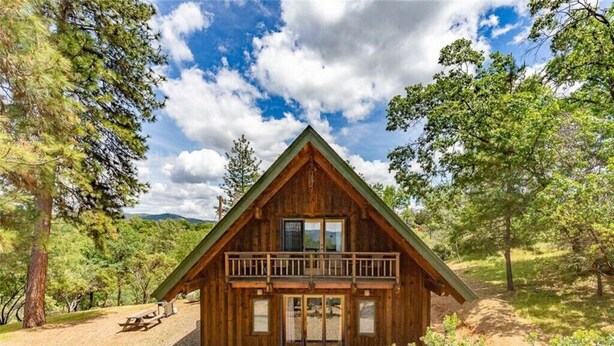 Eine Holzhütte mit Balkon, umgeben von Bäumen und blauem Himmel.