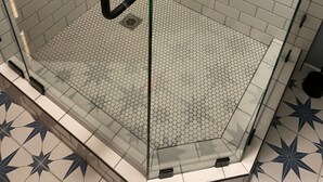 Eine gläserne Dusche mit weißen Fliesen im U-Bahn-Stil und einem sechseckigen Musterboden.