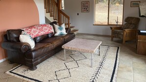 Ein Wohnzimmer mit braunem Ledersofa, einem Holzstuhl, einem Steintisch und einer Treppe, die zu einer anderen Ebene führt.