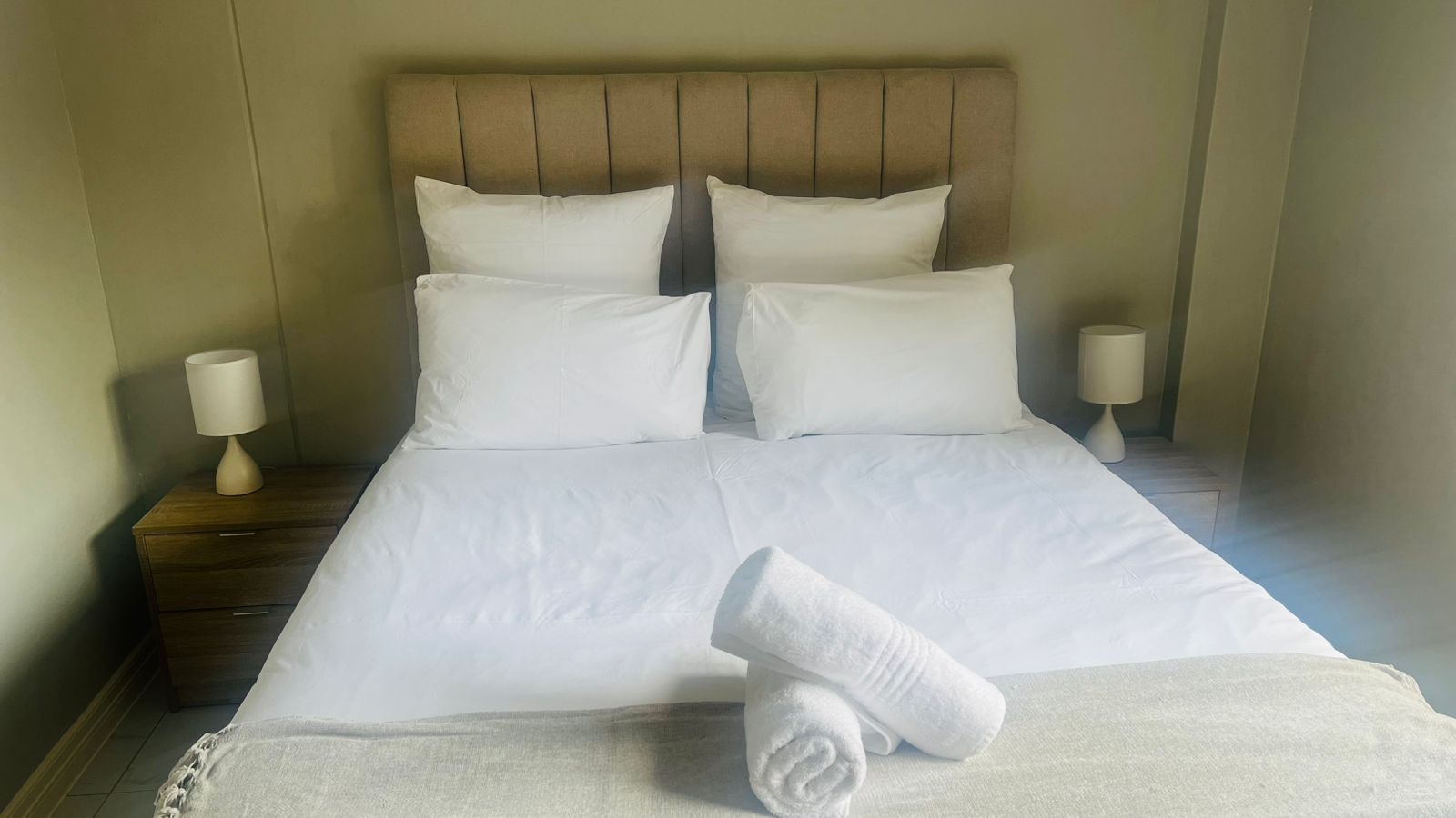 Une chambre d’hôtel avec un lit, deux tables de chevet et une serviette roulée posée sur le lit.
