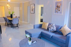 A modern living room with a grey sofa, a dining table with chairs, and a coffee table with a plant. - Sandton Westpoint Luxury Apartments (Sandton)