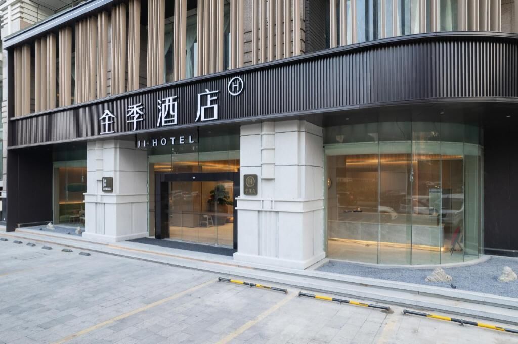 A hotel entrance with a modern facade, large glass windows, and a sign in a foreign language.