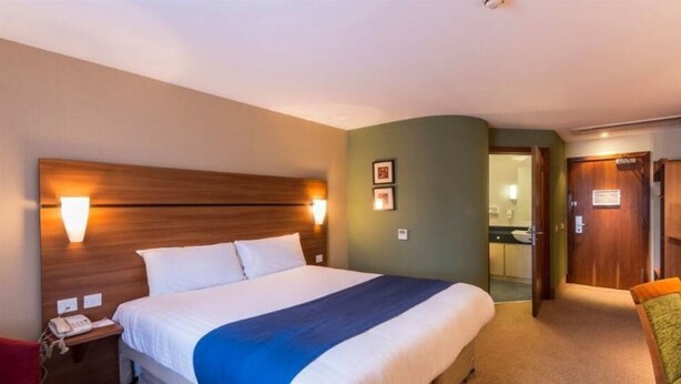 A hotel room with a large bed, bedside lamps, a wooden headboard, a chair, and a door leading to a bathroom. - Park Inn by Radisson Doncaster (Doncaster)