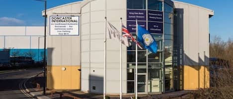 A modern building with a sign indicating it is Doncaster International, featuring amenities like air-conditioned bedrooms, a restaurant, bar, conference center, free parking, and free Wi-Fi.