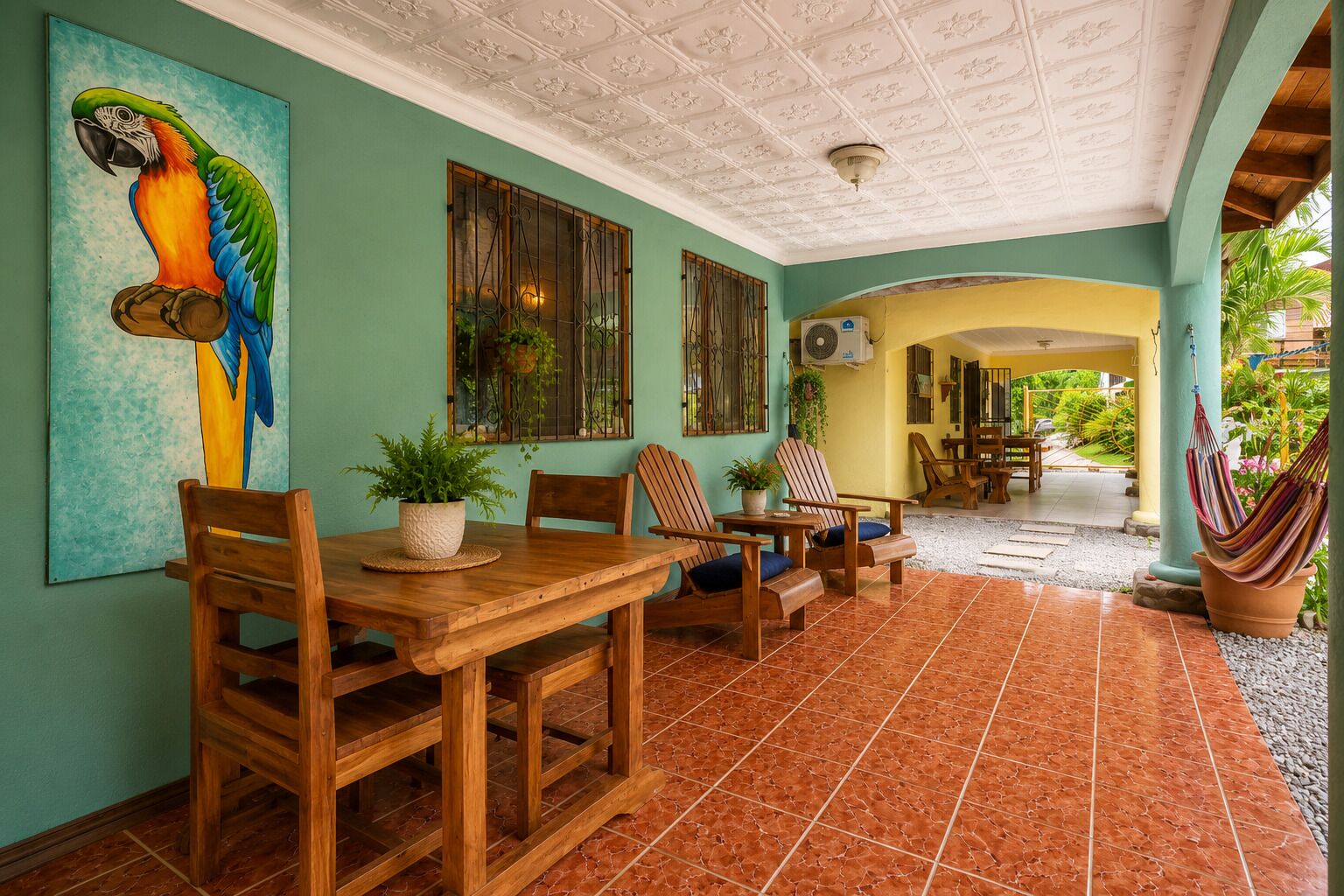 A dining area with wooden furniture, a parrot painting, and a view of the outdoor patio.