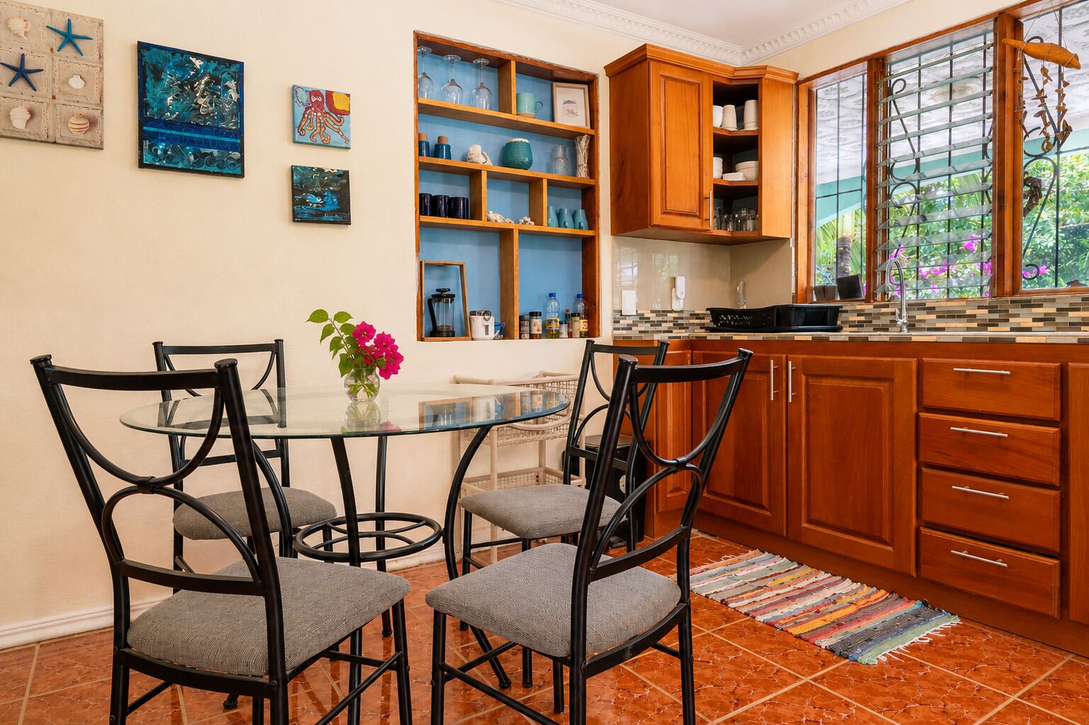 Una cocina con una mesa de comedor, sillas, armarios de madera y un ventanal con vistas a la vegetación.