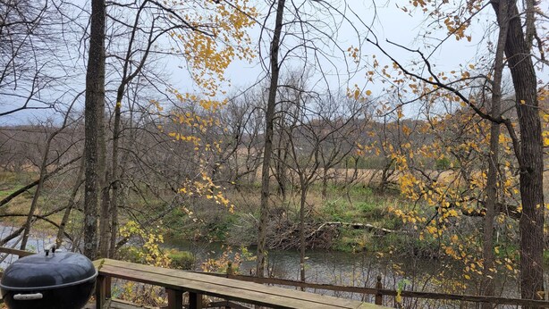 A wooden deck with a barbecue grill, overlooking a river and autumn foliage. - Blakley Hobbit Small Cabin (Viola)