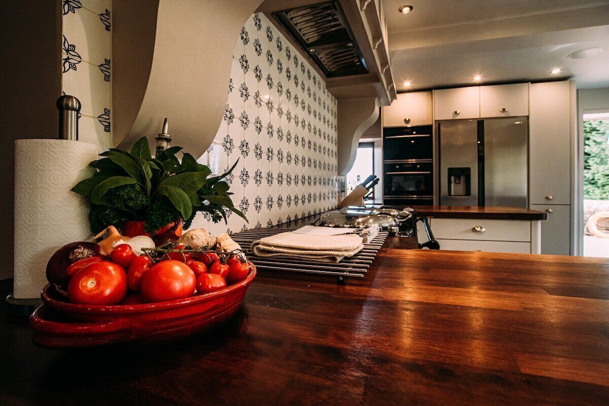 Een moderne keuken met een houten aanrecht, een kom met tomaten, een potplant en een behangetje met een patroon.