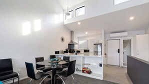 Una cucina moderna con mobili bianchi, un frigorifero in acciaio inossidabile e un forno integrato. C'è una zona pranzo con un tavolo rotondo e sedie nere.