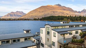 Un edificio moderno con tetto piatto e ampie finestre, con vista su un lago e montagne.