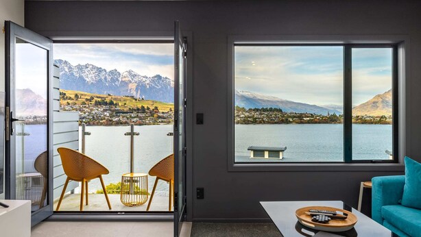 Una camera moderna con un'ampia porta scorrevole in vetro che si apre su un balcone con vista panoramica sulle montagne.