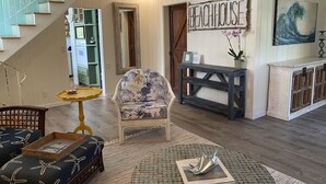 Ein Wohnzimmer mit Treppe, einem Sessel mit Blumenmuster, einem hölzernen Konsolentisch und einem Wandschild mit der Aufschrift 'BEACHHOUSE'.