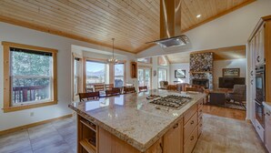 Une cuisine spacieuse dotée d’un grand îlot central, d’un plafond en bois et d’une cheminée en pierre.