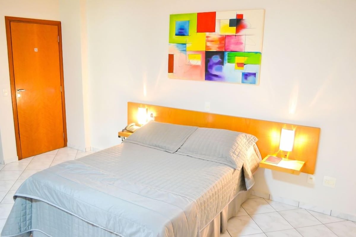 Ein Schlafzimmer mit einem Bett, Nachttischlampen, einem Wandbild und einer Tür.