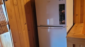 Une cuisine de taille réduite avec des murs en bois, un réfrigérateur blanc et une petite fenêtre équipée de stores.