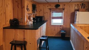 Une cuisine avec des murs en bois, un plan de travail noir et une fenêtre avec des stores.