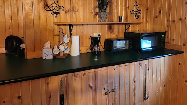 Une cuisine avec un lambris en bois, une machine à café, un grille-pain, un four à micro-ondes et une étagère ornée d’objets décoratifs.