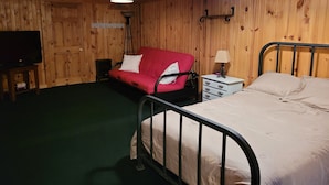 Une pièce comprenant un lit, un canapé rouge, une petite table, une lampe et un téléviseur.