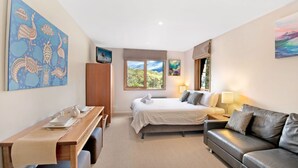 A hotel room with a bed, a desk, a leather sofa, and a window with a view of trees. - Les Perrieres Lodge - Spacious 3BR Luxury l Gym l Indoor Pool l Tennis l WiFi l BBQ (Crackenback)