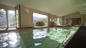An indoor swimming pool with clear water, large windows, and a view of mountains. - Les Perrieres Lodge - Spacious 3BR Luxury l Gym l Indoor Pool l Tennis l WiFi l BBQ (Crackenback)