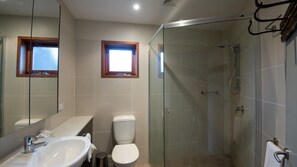 Ein modernes Badezimmer mit einer Duschkabine, einem großen Spiegel und einem Fenster über dem Waschbecken.