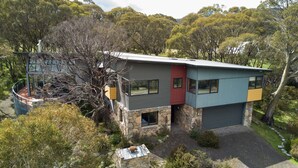 Una casa moderna de dos pisos con base de piedra, ventanas grandes y una combinación de paredes exteriores grises, rojas y azules.