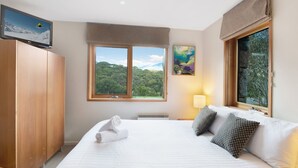 Habitación de hotel con una cama, televisión, ventana con vistas a árboles y un cuadro en la pared.