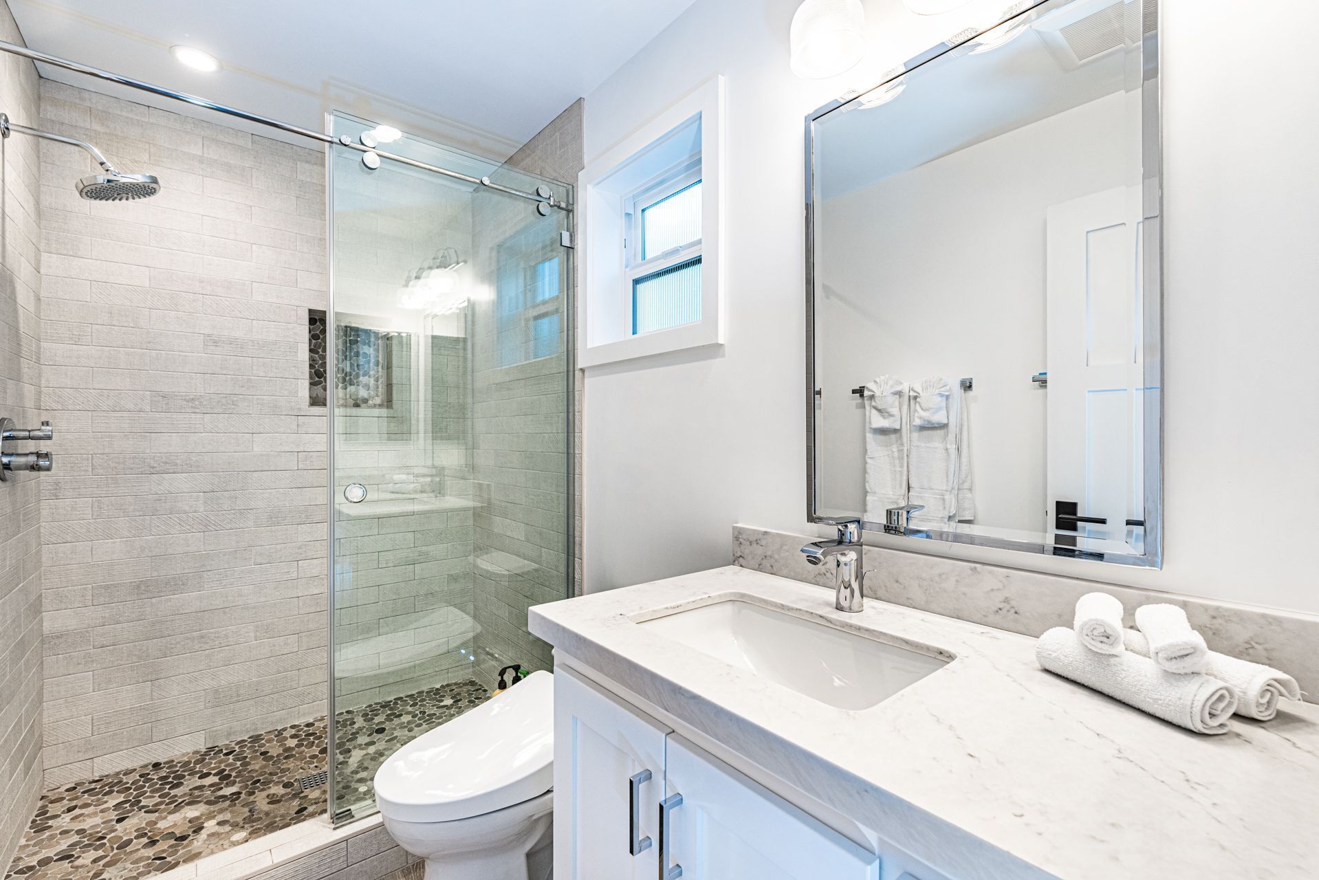 A modern bathroom with a glass-enclosed shower, a marble sink, and a large mirror.