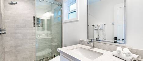A modern bathroom with a glass-enclosed shower, a marble sink, and a large mirror.