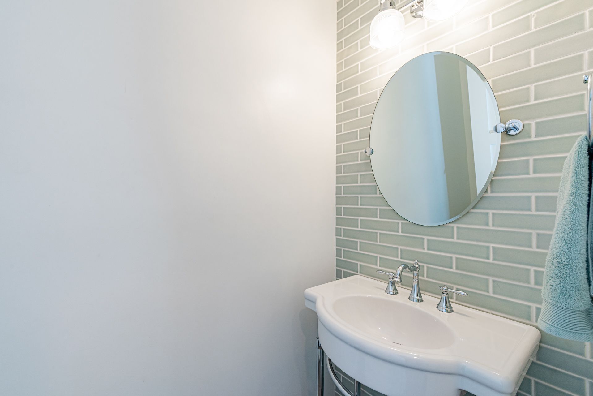 Ein Badezimmer mit einem weißen Waschbecken, einem runden Spiegel und einem Handtuch an der Wand.