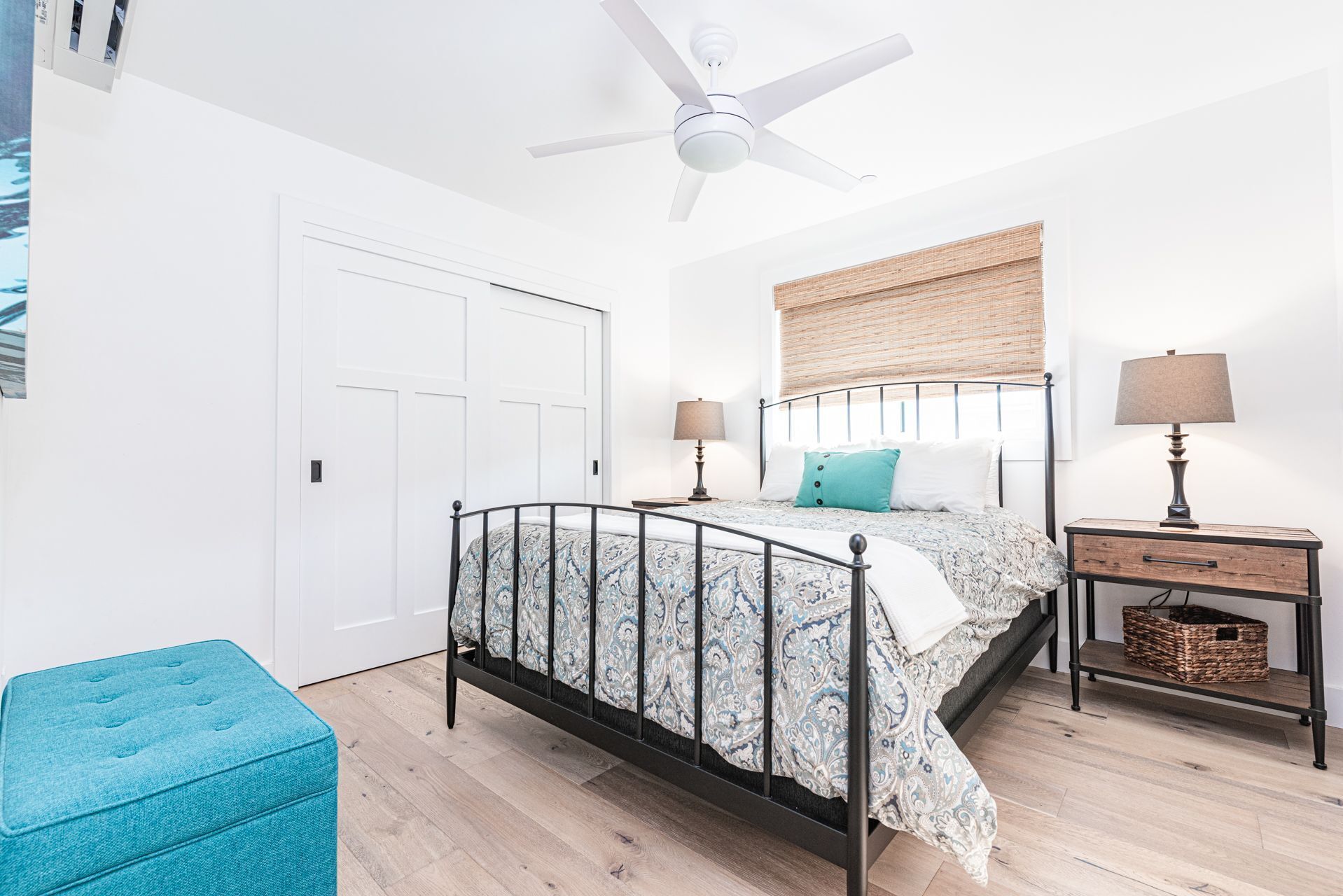 A bedroom with a bed, bedside tables, a ceiling fan, a window with blinds, and a door.