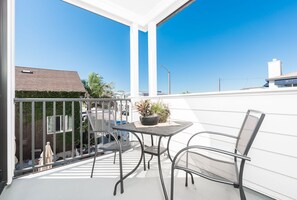 A balcony with a table and two chairs, a potted plant, and a view of the neighborhood.