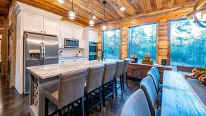 A modern kitchen with white cabinets, stainless steel appliances, and a large island with bar stools. - Tranquil Haven - Sleeps 21 - Modern Rustic Luxury Retreat Among the Pines! (Hochatown)