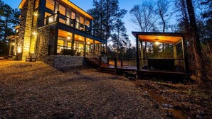 A modern two-story house with a stone facade, large windows, and a covered outdoor area. - Tranquil Haven - Sleeps 21 - Modern Rustic Luxury Retreat Among the Pines! (Hochatown)
