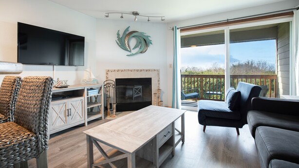 A living room with a fireplace, a television, and a balcony with a view. - Calypso at Nautilus (Ocean Shores)