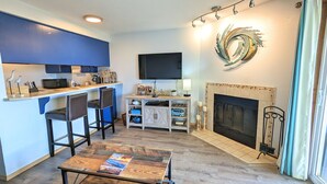 A compact living space with a kitchenette, a flat-screen TV, a fireplace, and a small dining area. - Calypso at Nautilus (Ocean Shores)