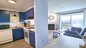 A modern kitchen with blue cabinets, a microwave, and a stove. There is a dining area with a table and chairs, and a fireplace. - Calypso at Nautilus (Ocean Shores)