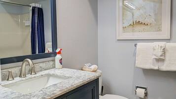 A bathroom with a marble sink, dark cabinets, a white toilet, and a framed artwork on the wall.
