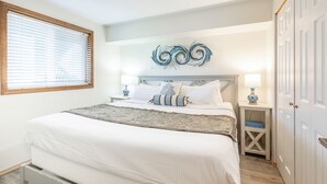 A neatly made bed with a decorative headboard, a bedside table with a lamp, and a wardrobe. - Calypso at Nautilus (Ocean Shores)
