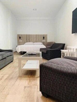 Una habitación de hotel moderna con una cama, dos sofás, una mesa de centro y un televisor fijado a la pared.