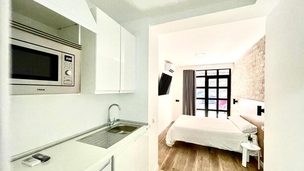 Une chambre d’hôtel compacte comprenant un coin cuisine, un lit, une petite table de chevet et un téléviseur.