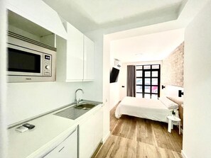 Una habitación de hotel compacta con kitchenette, una cama, una mesita de noche pequeña y un televisor.