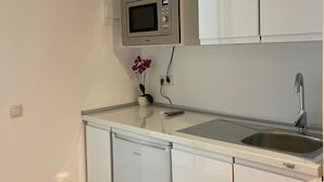 Une cuisine compacte avec des meubles blancs, un four à micro-ondes, un évier et une petite orchidée en pot.