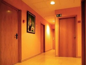 Un couloir d’hôtel avec des portes en bois, un tableau encadré au mur et un panneau indiquant la sortie.