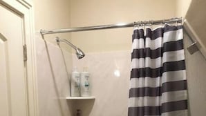 A bathroom with a shower curtain, a bathtub, and a shelf with toiletries. - The "Crash Pad" Studio Apartment in Downtown Provo (Provo)