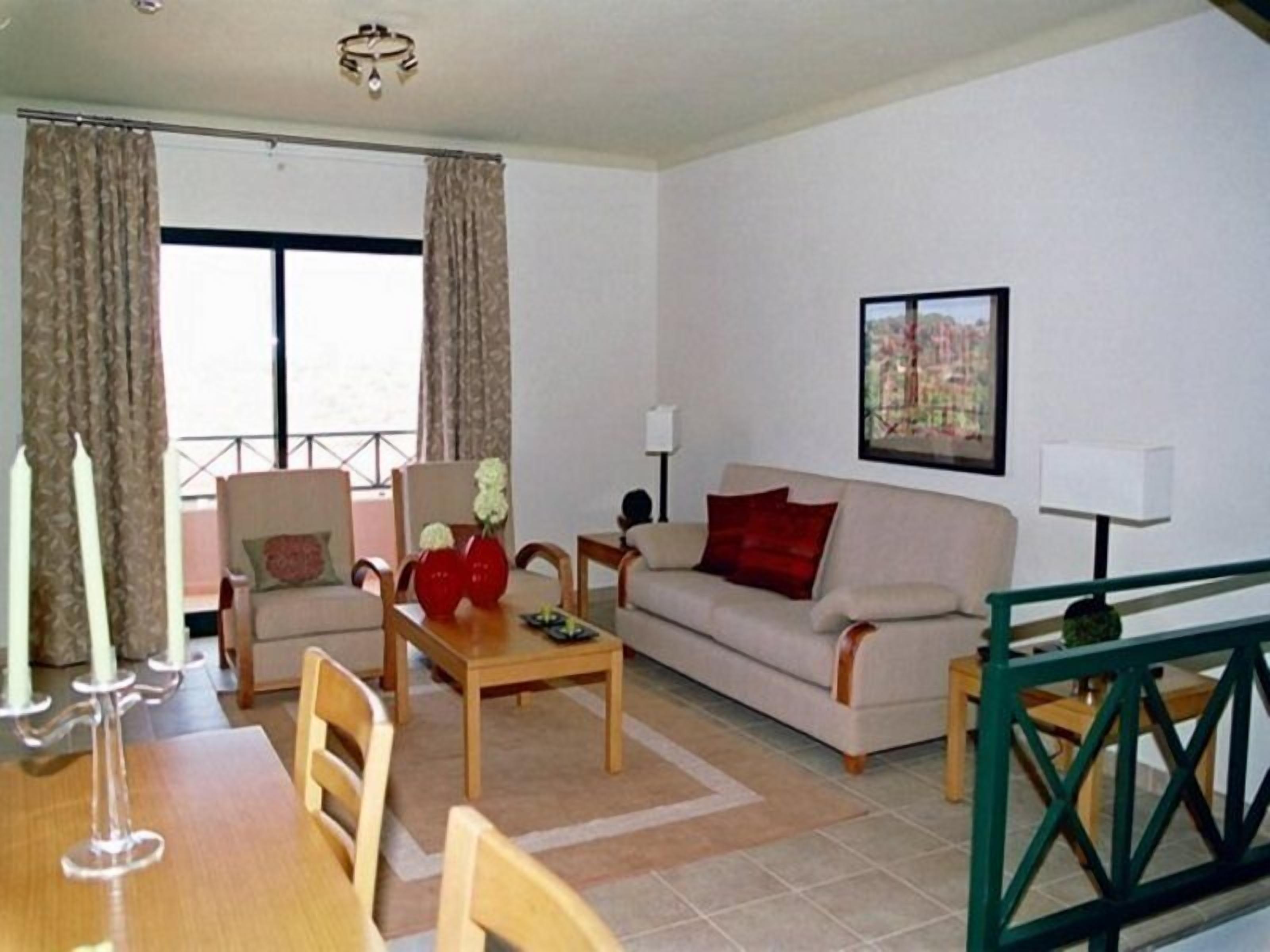 A living room with a sofa, chairs, a table, and a balcony with curtains.